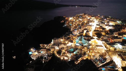 Aerial drone night shot of beautiful illuminated traditional and picturesque village of Oia built on a cliff, Santorini island, Cyclades, Greece © aerial-drone