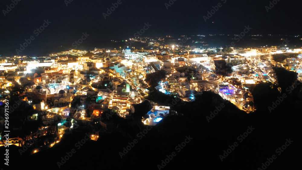 Aerial drone night shot of beautiful illuminated traditional and picturesque village of Oia built on a cliff, Santorini island, Cyclades, Greece