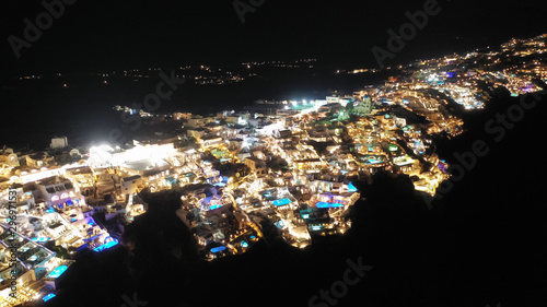 Aerial drone night shot of beautiful illuminated traditional and picturesque village of Oia built on a cliff, Santorini island, Cyclades, Greece