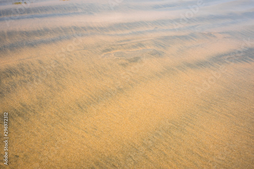 Beach sand texture. Golden yellow color background. Sand surface of a beach with clear sea water. Waves. 