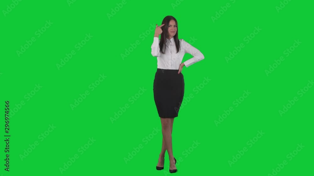 Young displeased business woman showing finger crazy gesture pointing at temple. Full body isolated on green screen chroma key background Young displeased business woman showing finger crazy gesture pointing at temple. Full body isolated on green screen chroma key background