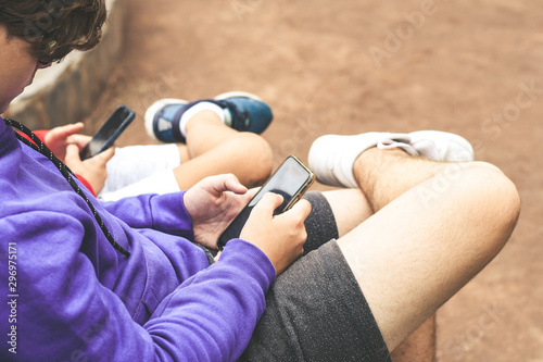 Close up view of a couple of teen using smartphone sitting outdoor at the park. Teenagers communicate with new technology devices with remote friends. Youth, new tech trend and communication concept. © Fabio Principe