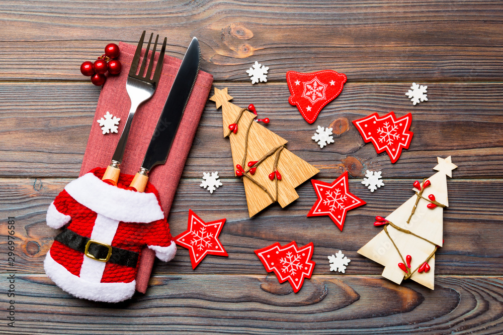 Fototapeta premium Top view of fork and knife tied up with ribbon on napkin on wooden background. Close up of christmas decorations and New Year tree. Happy holiday concept
