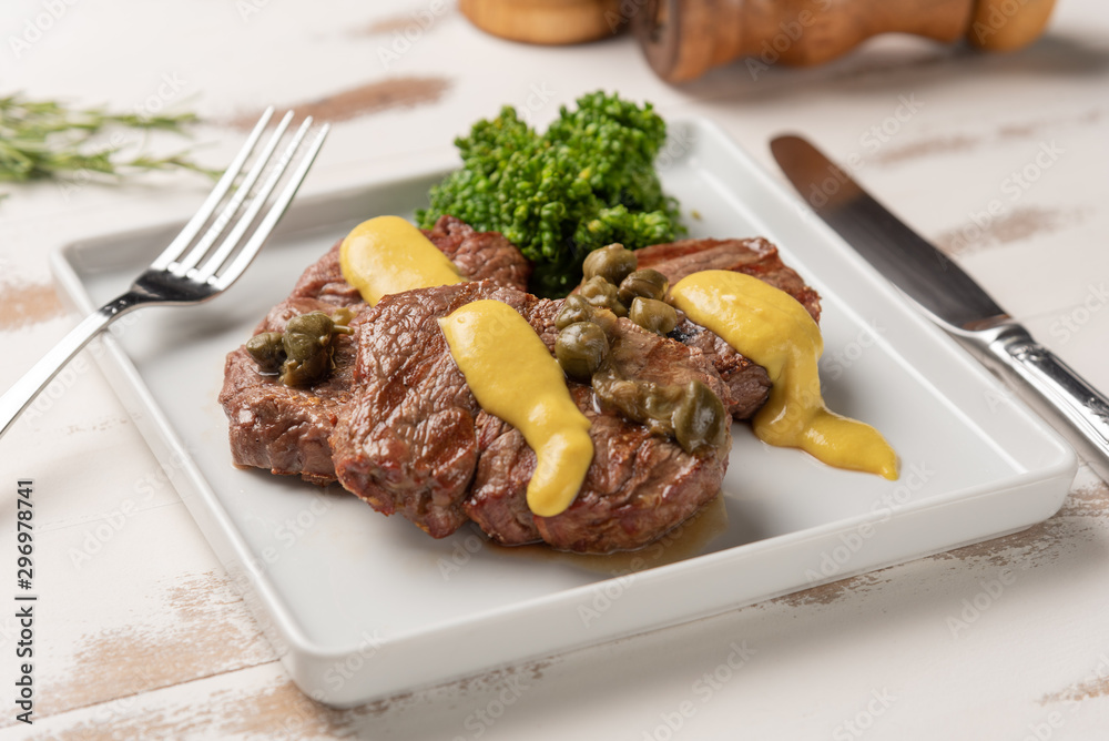 Filet mignon with caper and mustard sauce, broccoli, pepper grinder on wooden white background, soft light