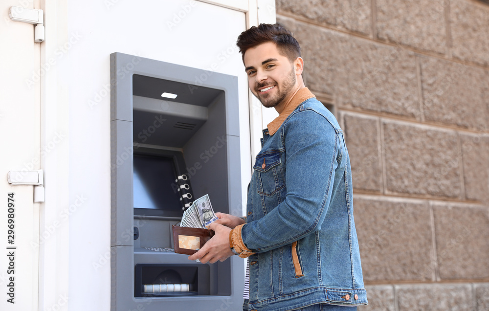 Young man with money near cash machine outdoors Young man with money near cash machine outdoors