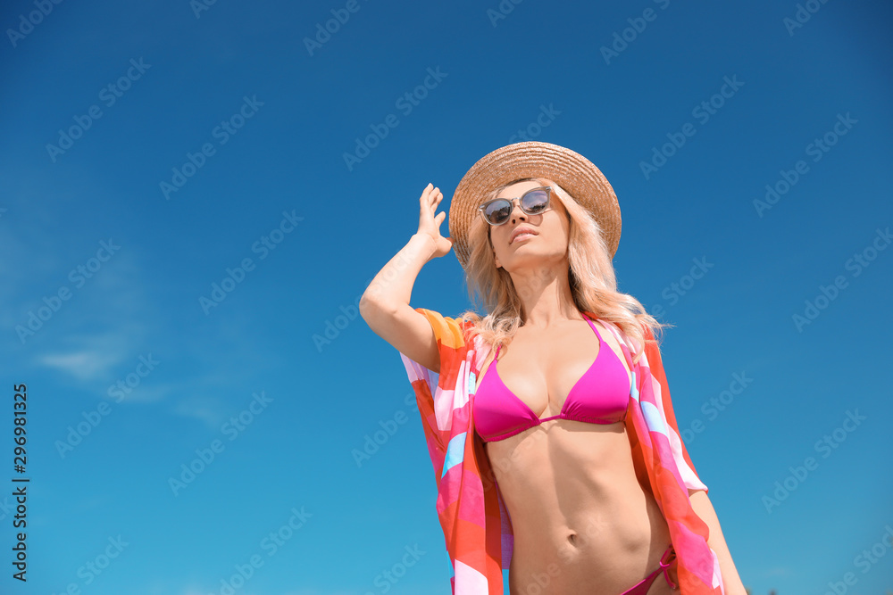 Sexy young woman in stylish bikini and cover up with accessories against blue sky on sunny day, low angle view. Space for text Sexy young woman in stylish bikini and cover up with accessories against blue sky on sunny day, low angle view. Space for text