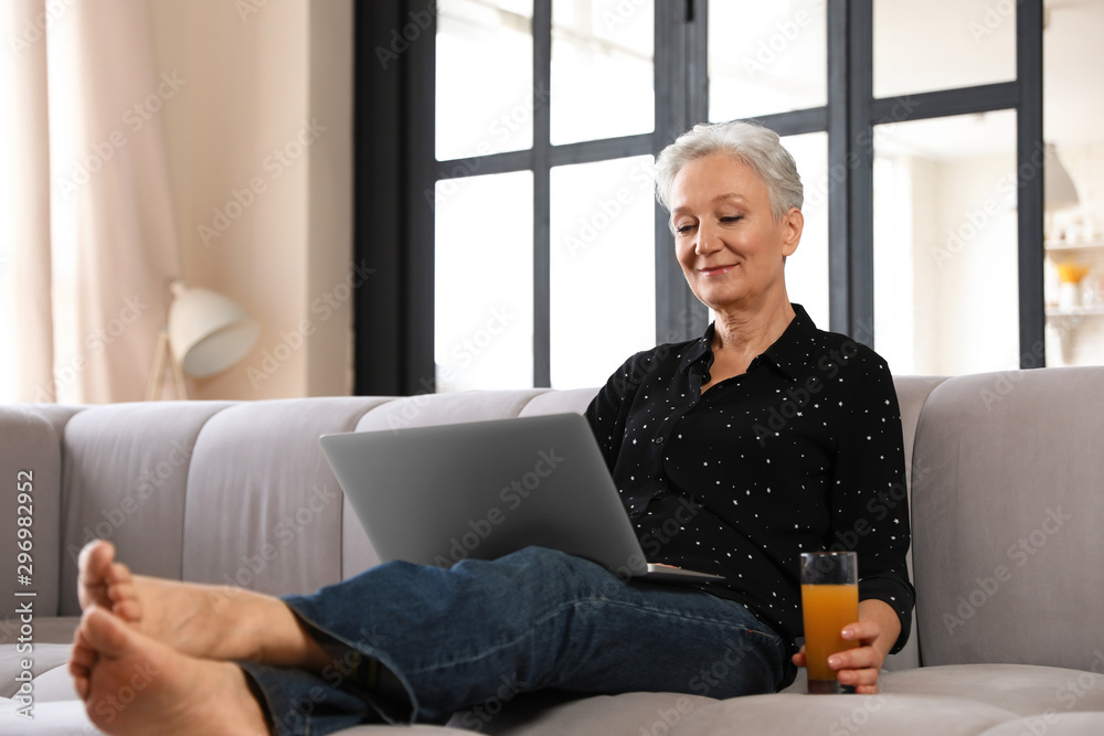 Mature woman with laptop and drink sitting on sofa at home. Smart aging Mature woman with laptop and drink sitting on sofa at home. Smart aging