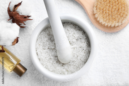 Mortar and pestle with sea salt for spa scrubbing procedure on white fabric  flat lay