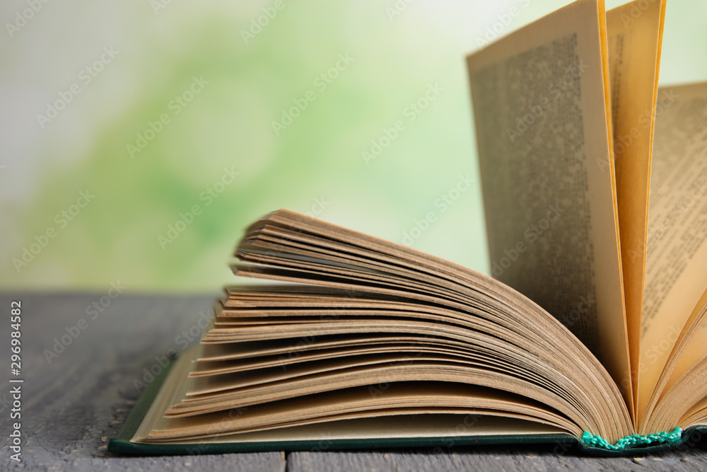 Open book on grey wooden table against blurred green background, closeup Open book on grey wooden table against blurred green background, closeup