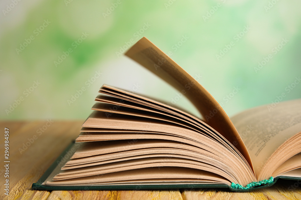 Open book on wooden table against blurred green background, closeup Open book on wooden table against blurred green background, closeup