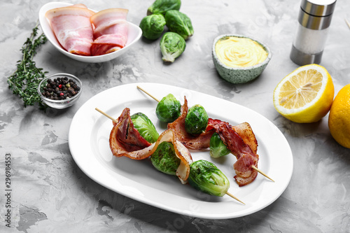 Skewers with Brussels sprouts and bacon in plate on grey table