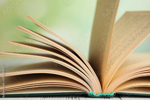 Open book on white wooden table against blurred green background, closeup