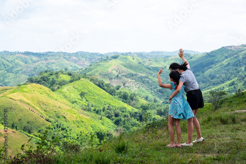 Happy asian family mother and daughter standing on top of beautiful mountain holding raised hands