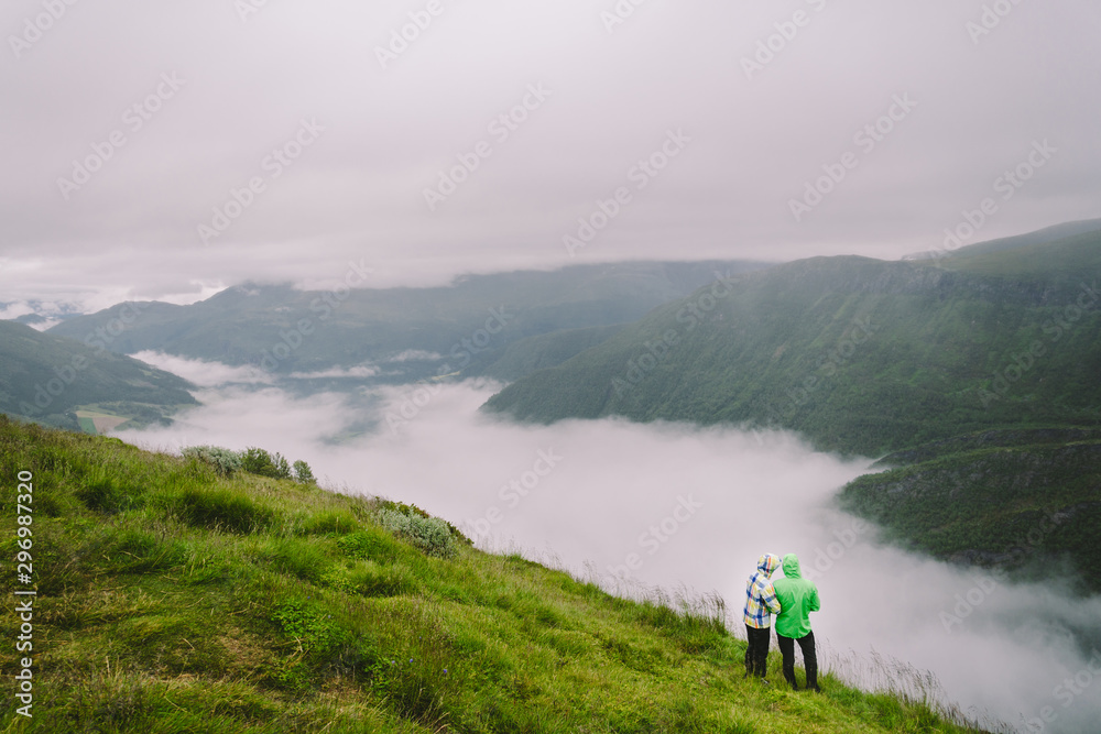 Hiking in Norway. Romantic couple of tourists on the edge of cliff looking on beautiful scenery. Back view of couple hugging at observation deck with panoramic view. Traveling together, adventure