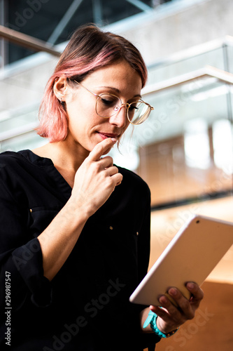 Beautiful young Caucasian woman, girl or student with hipster style and eyeglasses thinking and questioning herself in front of her tablet. Technology app photography