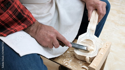 Traditional handicraft woodworking or hobby. An elderly man cuts a spoon out of a wooden block with a sharp chisel. Men's hands with a tool closeup.