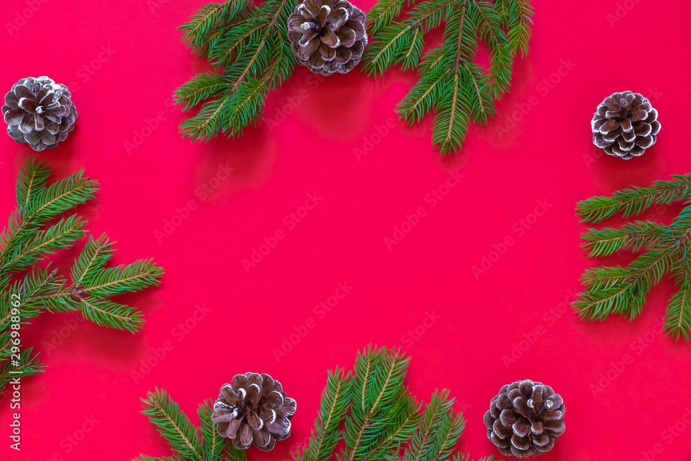 Fototapeta premium Christmas flat lay on red background with green pine branches and pine cones. Image with copy space, top view