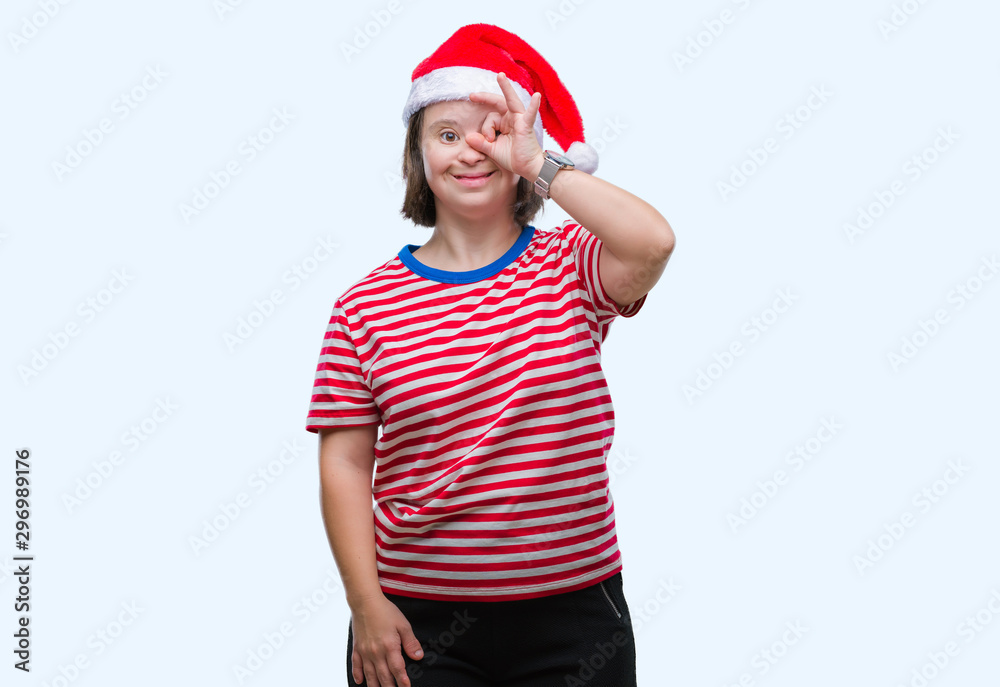 Young adult woman with down syndrome wearing christmas hat over isolated background doing ok gesture with hand smiling, eye looking through fingers with happy face. Young adult woman with down syndrome wearing christmas hat over isolated background doing ok gesture with hand smiling, eye looking through fingers with happy face.