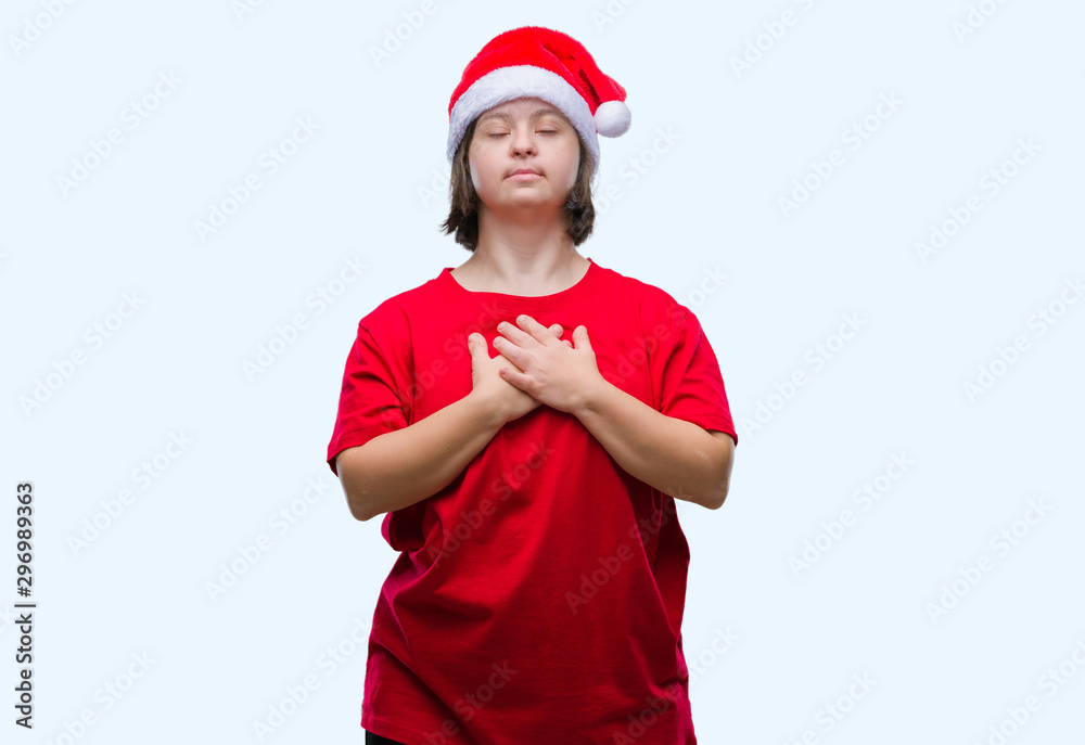 Young adult woman with down syndrome wearing christmas hat over isolated background smiling with hands on chest with closed eyes and grateful gesture on face. Health concept. Young adult woman with down syndrome wearing christmas hat over isolated background smiling with hands on chest with closed eyes and grateful gesture on face. Health concept.