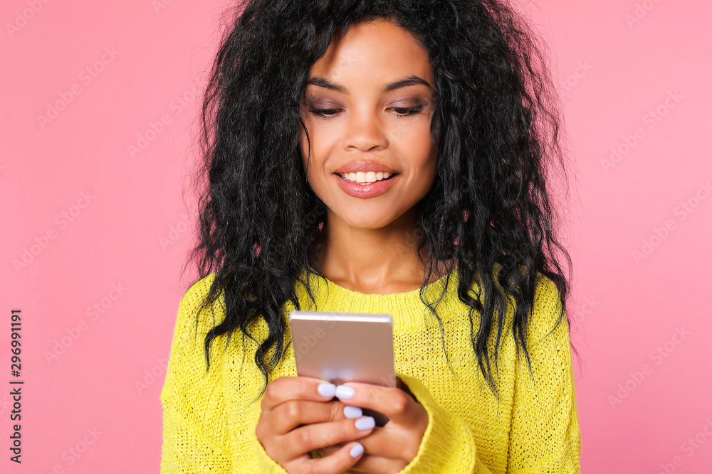 Interesting information. Concentrated African ethnic woman in yellow sweater is looking at the screen of her smartphone and smiling, while reading or watching something. Interesting information. Concentrated African ethnic woman in yellow sweater is looking at the screen of her smartphone and smiling, while reading or watching something.