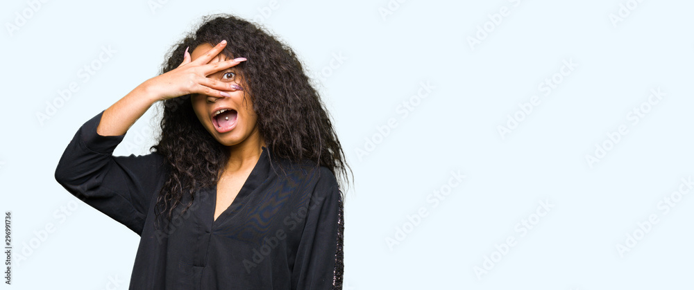 Young beautiful girl with curly hair wearing elegant dress peeking in shock covering face and eyes with hand, looking through fingers with embarrassed expression. Young beautiful girl with curly hair wearing elegant dress peeking in shock covering face and eyes with hand, looking through fingers with embarrassed expression.