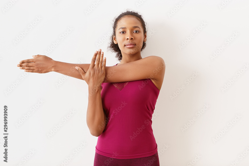 Horizintal shot of attractive athletic young dark skinned female in sportswear stretching arm muscles after cardio workout, having confident facial expression. Fitness, active and healthy lifestyle Horizintal shot of attractive athletic young dark skinned female in sportswear stretching arm muscles after cardio workout, having confident facial expression. Fitness, active and healthy lifestyle
