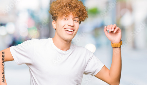 Young handsome man with afro hair wearing casual white t-shirt Dancing happy and cheerful, smiling moving casual and confident listening to music