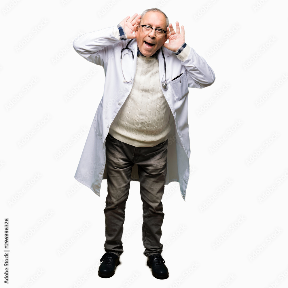 Handsome senior doctor man wearing medical coat Trying to hear both hands on ear gesture, curious for gossip. Hearing problem, deaf Handsome senior doctor man wearing medical coat Trying to hear both hands on ear gesture, curious for gossip. Hearing problem, deaf