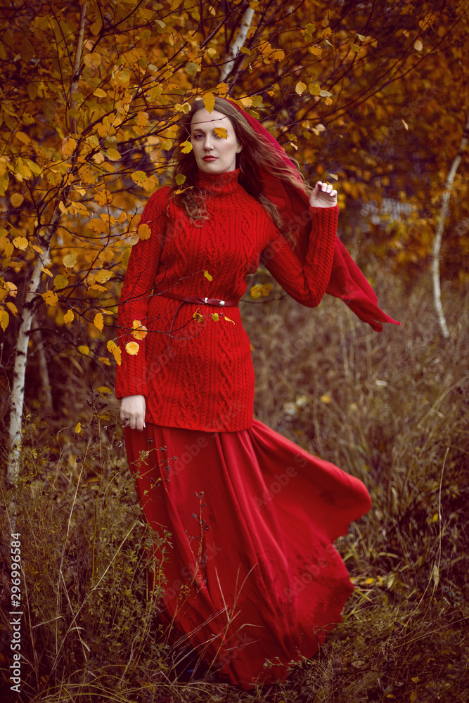 girl in a red dress and sweater stands in a field with trees girl in a red dress and sweater stands in a field with trees