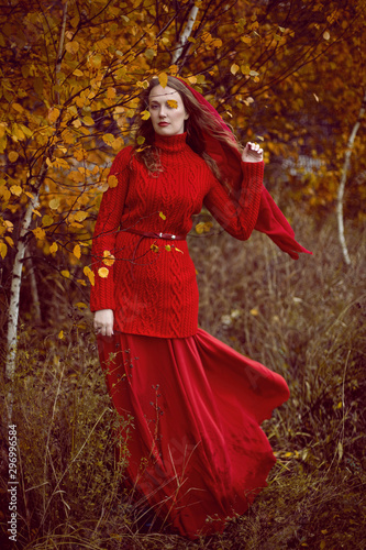 girl in a red dress and sweater stands in a field with trees