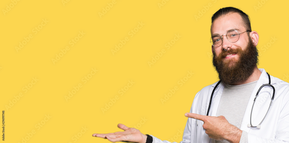 Young blond doctor man with beard wearing medical coat amazed and smiling to the camera while presenting with hand and pointing with finger. Young blond doctor man with beard wearing medical coat amazed and smiling to the camera while presenting with hand and pointing with finger.