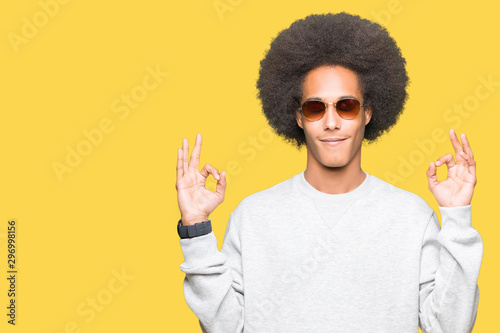 Young african american man with afro hair wearing sunglasses relax and smiling with eyes closed doing meditation gesture with fingers. Yoga concept.
