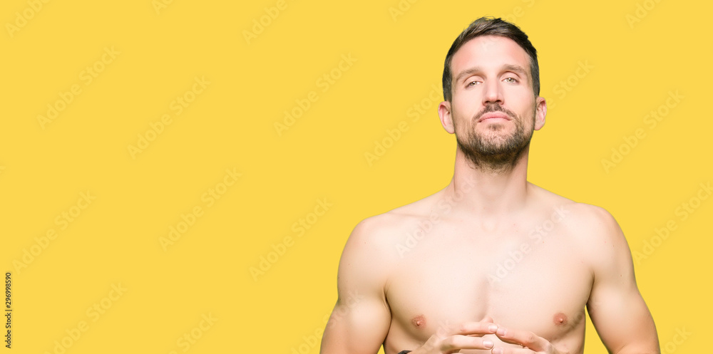 Handsome shirtless man showing nude chest Hands together and fingers crossed smiling relaxed and cheerful. Success and optimistic