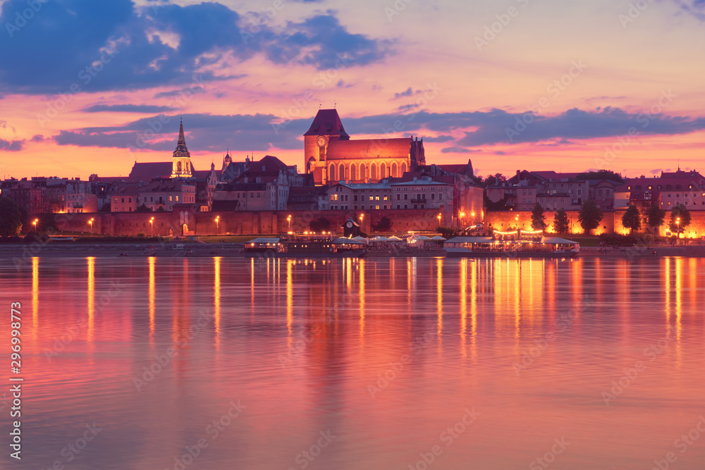 Torun old town in Poland, UNESCO world heritage site, with illumination, reflected in Vistula river on sunset sunset.