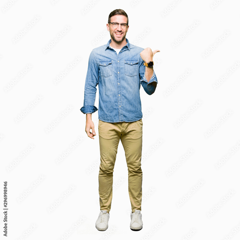 Handsome man wearing glasses smiling with happy face looking and pointing to the side with thumb up. Handsome man wearing glasses smiling with happy face looking and pointing to the side with thumb up.