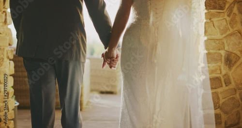Bride and groom walking together holding hands on their wedding day, medium detail shot of married couple holding hands at sunset photo