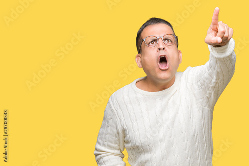 Middle age arab man wearing glasses over isolated background Pointing with finger surprised ahead, open mouth amazed expression, something in front