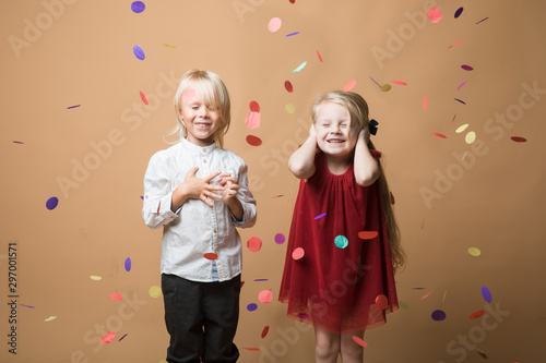 a boy and a girl stand on an orange background with their hands over their ears and shout from a confetti firecracker