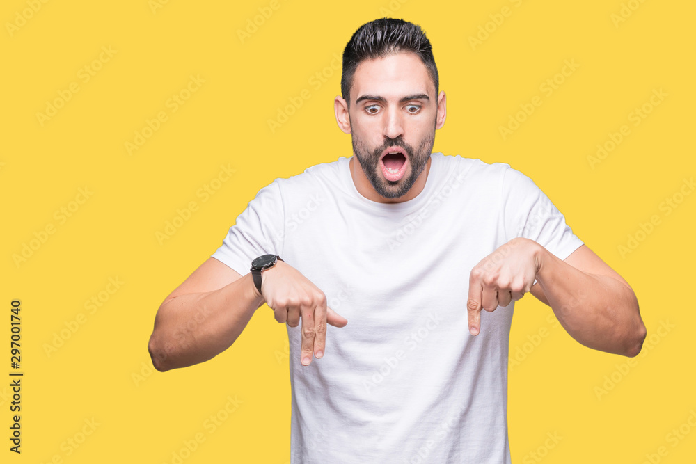 Handsome man wearing white t-shirt over yellow isolated background Pointing down with fingers showing advertisement, surprised face and open mouth Handsome man wearing white t-shirt over yellow isolated background Pointing down with fingers showing advertisement, surprised face and open mouth