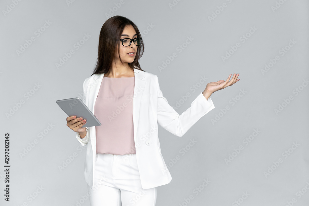 Young adult indian businesswoman in white formal wear standing isolated on grey background with copy space. Woman with tablet computer looking away, holding invisible object copy space on hand Young adult indian businesswoman in white formal wear standing isolated on grey background with copy space. Woman with tablet computer looking away, holding invisible object copy space on hand