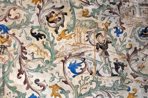 Fragment of the ancient castle wall. There is a fresco on the wall. The painting shows a man, a dog, plants.