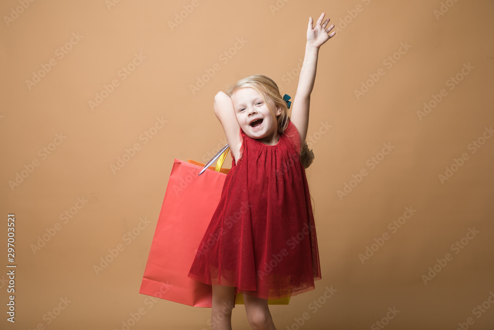 A young girl in a red dress and with shopping bags, very happy shopping. A young girl stands on an orange background