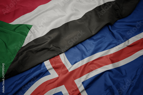 waving colorful flag of iceland and national flag of sudan.