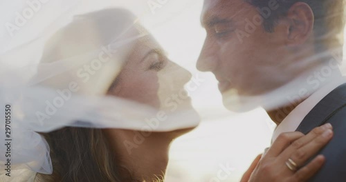 Intimate close up shot of a multi ethnic bride and groom smiling and looking at one and other underneath a white veil, intimate marriage ceremony at sunset photo