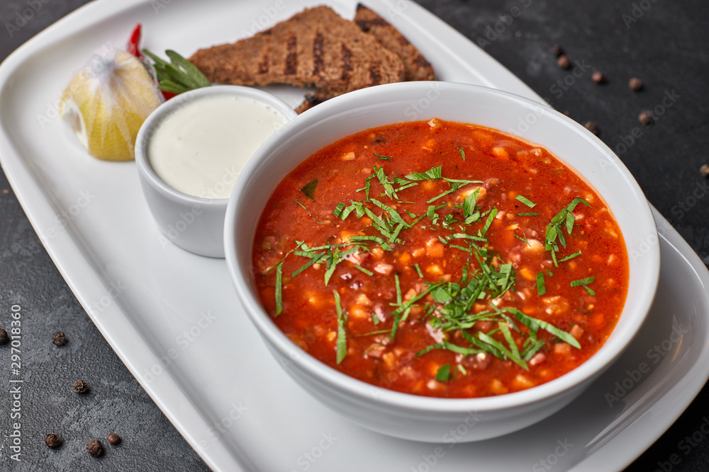 Red borscht on a white plate with bread and sour cream, on a dark background Red borscht on a white plate with bread and sour cream, on a dark background
