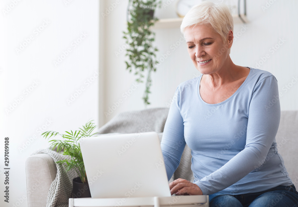 Cheerful senior lady using laptop on sofa at home Cheerful senior lady using laptop on sofa at home