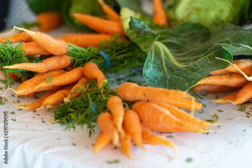 Carrots bunched with the stalks attached on a white tablecloth. The bright orange vegetables are clean and pointy with deep green stalks. 