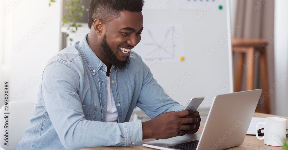 Happy black manager looking at smartphone screen reading pleasant message Happy black manager looking at smartphone screen reading pleasant message