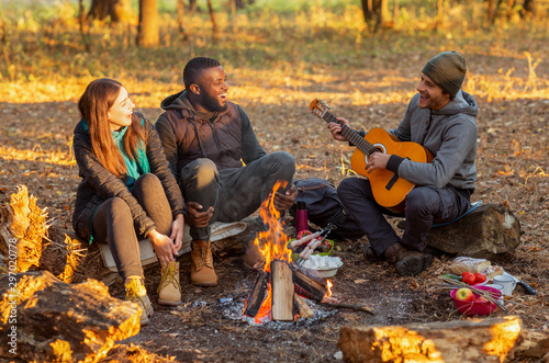 Group of people camping and singing in autumn woods