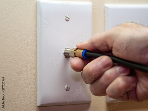Male electrician connecting coax cable cord to wall outlet. Coaxial wire connection for TV and high speed broadband internet. Television service installation.